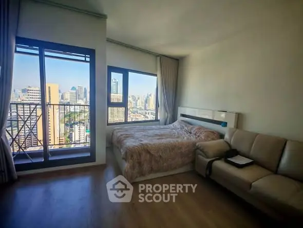 Modern bedroom with city view and balcony access in high-rise apartment.