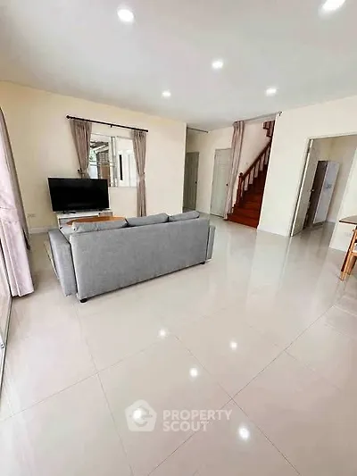 Spacious living room with modern decor and natural light, featuring a cozy gray sofa and sleek tiled flooring.