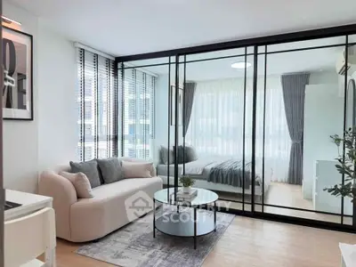 Modern open-plan living room with glass partition to bedroom, featuring stylish decor and natural light.