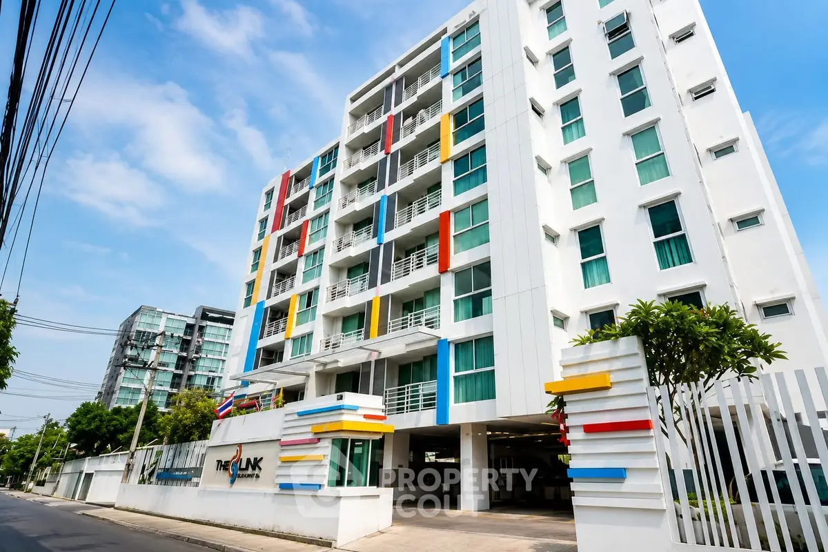 Modern multi-story apartment building with colorful accents and lush greenery.