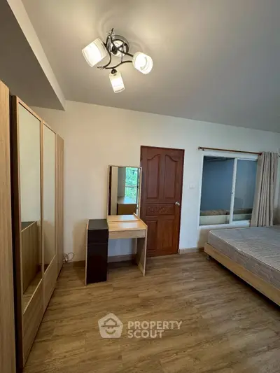 Spacious bedroom with wooden flooring, modern wardrobe, and elegant lighting.