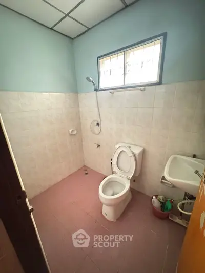 Simple bathroom with toilet, sink, and shower in a tiled setting.