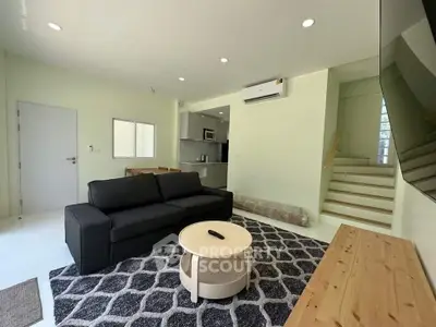 Modern living room with sleek black sofa, stylish rug, and open kitchen layout in a contemporary home.