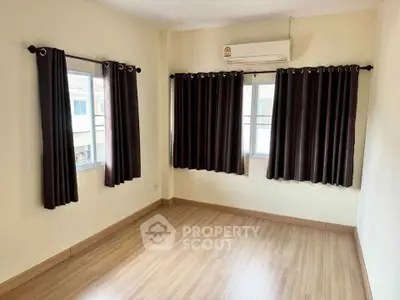 Spacious bedroom with wooden flooring and large windows for natural light.