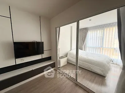 Modern bedroom with glass partition and mounted TV, featuring sleek design and natural light.