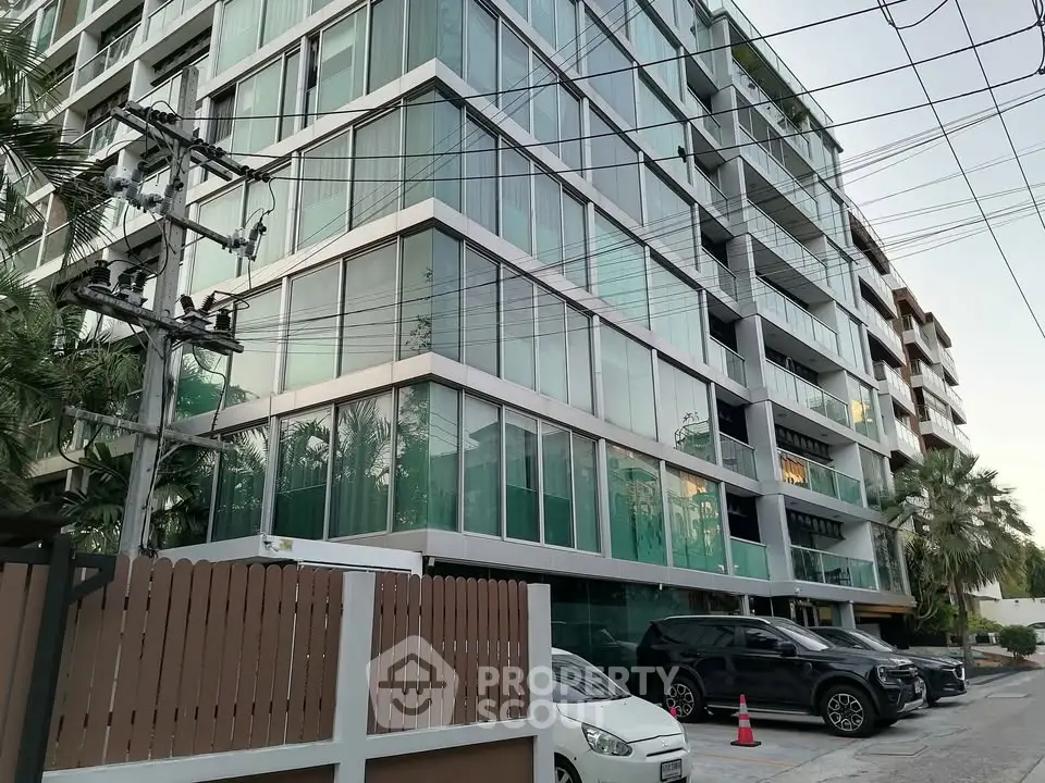 Modern condominium building with glass facade and parked cars in urban setting.