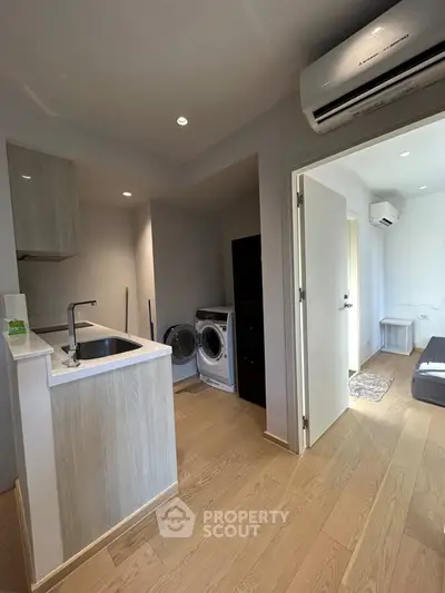 Modern apartment interior with kitchen and laundry area, featuring sleek design and wooden flooring.