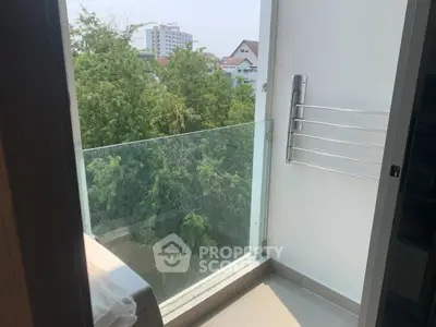 Charming balcony with glass railing offering lush green views, perfect for relaxation.