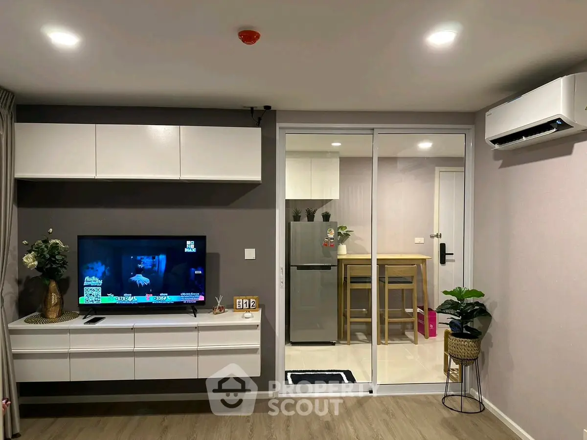 Modern living room with sleek TV unit and view into stylish kitchen.