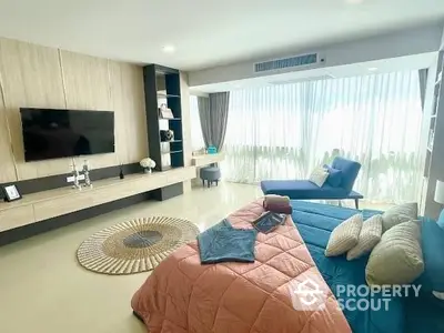 Spacious living room with modern design, featuring a large blue sofa, sleek entertainment unit, and floor-to-ceiling windows draped with sheer curtains.