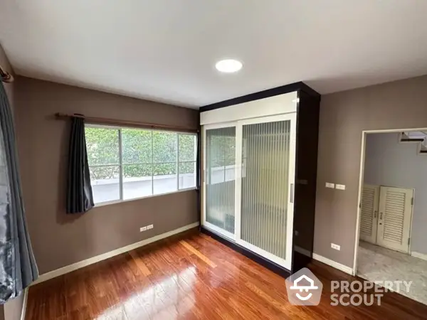 Spacious living room with polished hardwood floors, large windows for natural light, and direct access to a cozy balcony, perfect for relaxation.