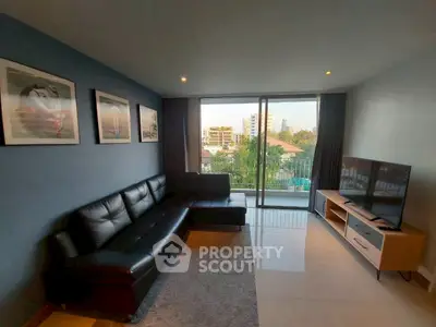 Modern living room with sleek black sofa and large TV, featuring a balcony with city view.