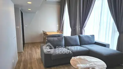 Modern living room with cozy gray sofa and dining area, featuring large windows and elegant curtains.