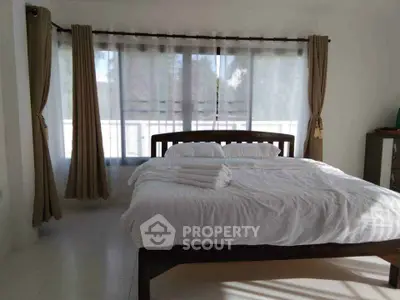 Spacious bedroom with large windows and elegant curtains, featuring a comfortable bed with fresh linens.