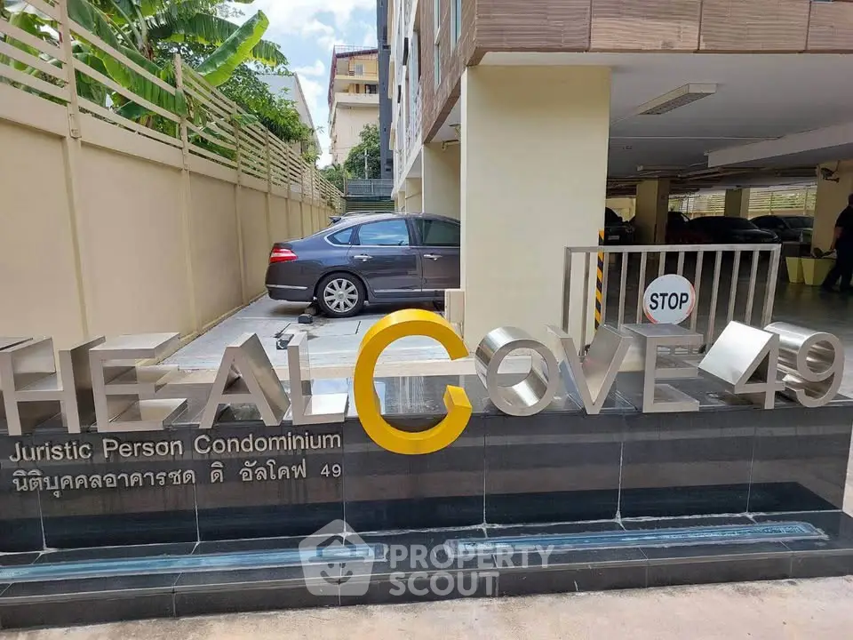 Modern condominium entrance with sleek signage and parking area, showcasing urban living convenience.