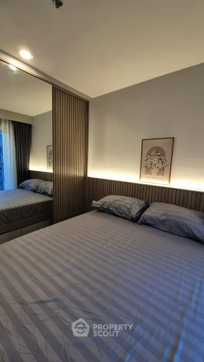 Modern bedroom with stylish lighting and mirrored wardrobe in a cozy apartment.