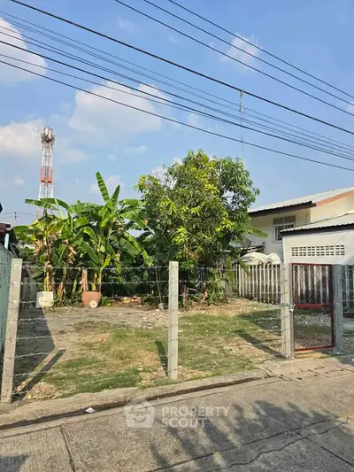 Vacant land plot with potential for development in a residential area, featuring a fenced boundary and lush greenery.