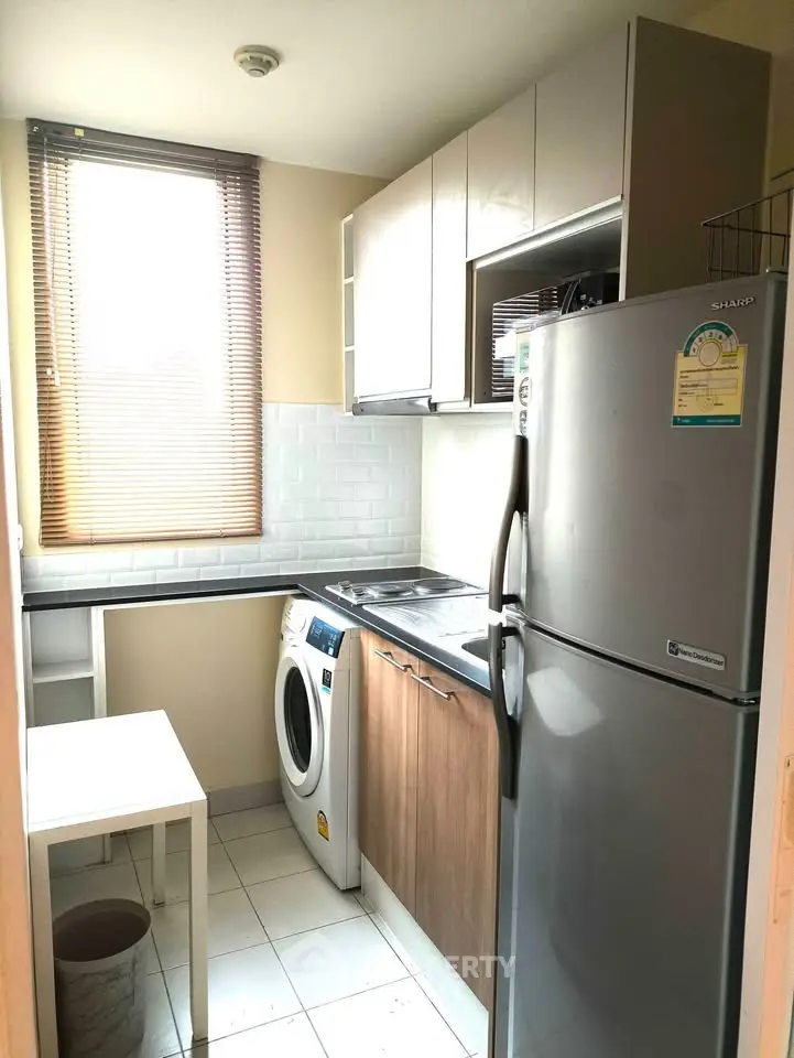 Compact kitchen with modern appliances, washing machine, and ample natural light from large window.
