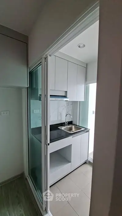 Compact modern kitchen with sleek cabinetry and glass sliding door in a stylish apartment.