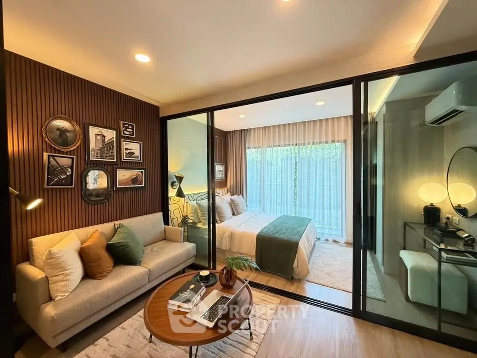 Modern bedroom with glass partition and cozy living area, featuring stylish decor and natural light.