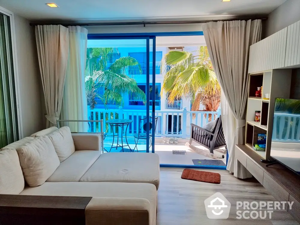 Spacious and inviting living room with plush sofa and direct access to a sunlit balcony with tropical palm views, perfect for relaxation and entertaining guests.