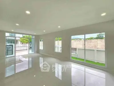 Spacious modern living room with large windows and glossy tiled floors, offering abundant natural light.