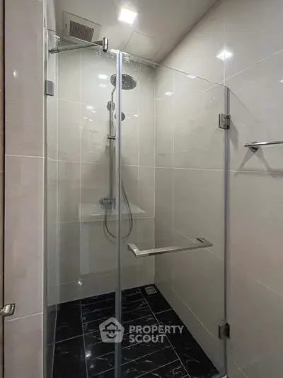 Modern glass-enclosed shower in sleek bathroom with black tile floor.