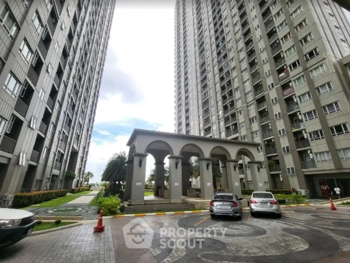 Modern high-rise residential building with landscaped entrance and parking area.