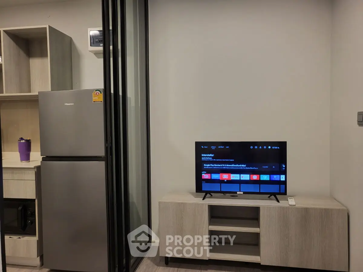 Modern apartment interior with sleek kitchen and cozy living area featuring a TV and stylish cabinetry.