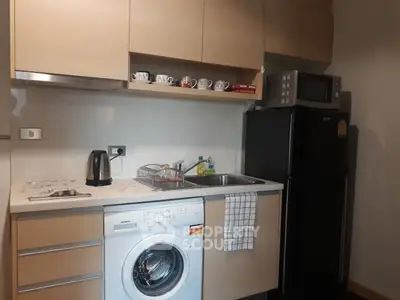 Modern kitchen with washing machine, microwave, and fridge in compact layout.