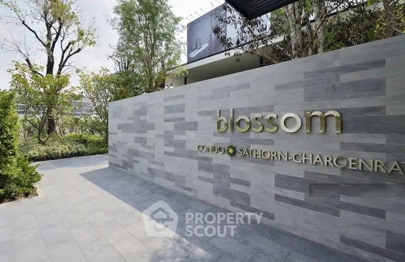 Modern condo entrance with stylish stone wall and lush greenery at Blossom Condo Sathorn-Charoenrat.