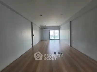 Spacious empty room with wooden flooring and large window, ideal for customization.