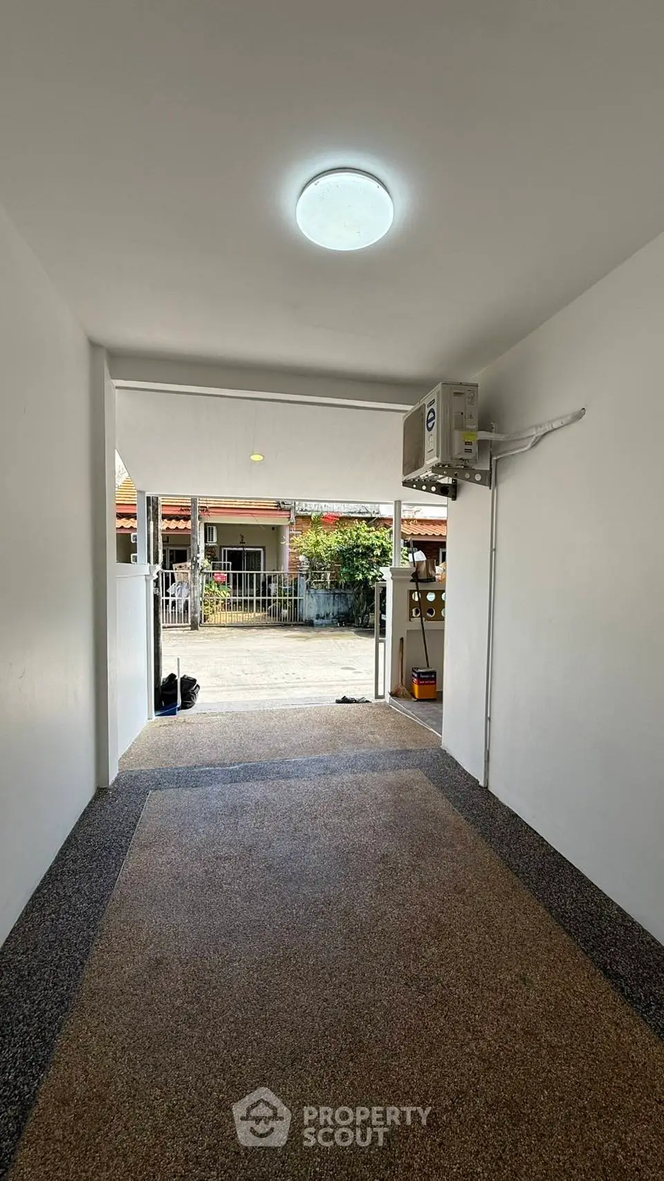 Covered entrance with modern lighting and textured flooring leading to residential area.