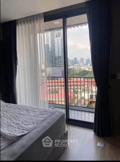 Modern bedroom with city view and balcony access in high-rise apartment.