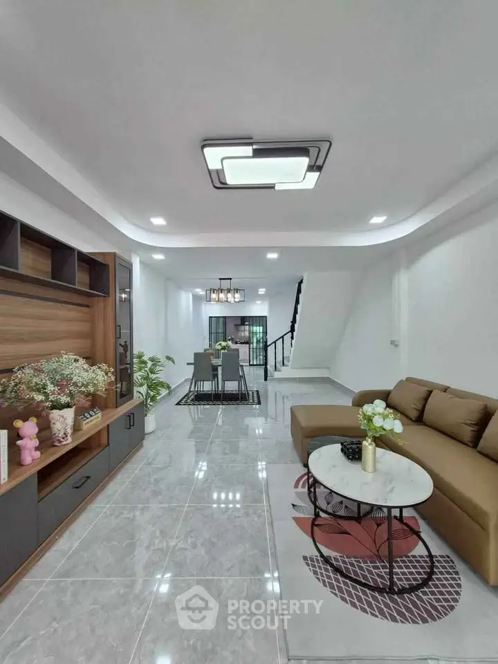 Modern living room with stylish decor and open dining area, featuring sleek furniture and elegant lighting.