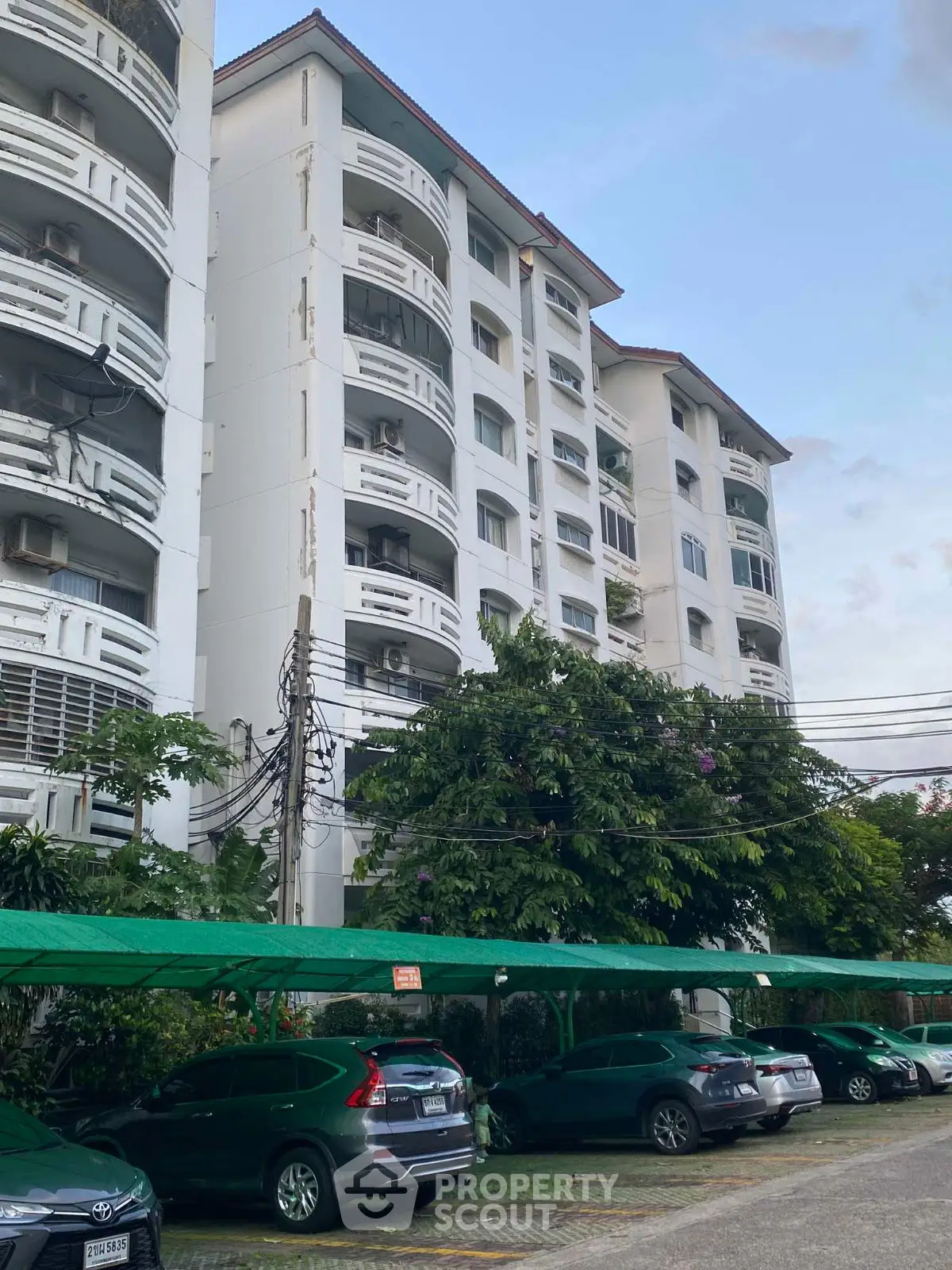 Charming residential building with lush greenery and covered parking, ideal for urban living.