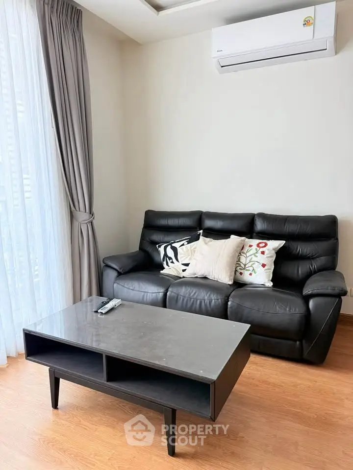Modern living room with black leather sofa and sleek coffee table, featuring elegant decor and natural light.