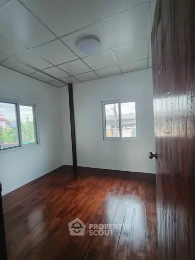 Spacious bedroom with wooden flooring and ample natural light from large windows.