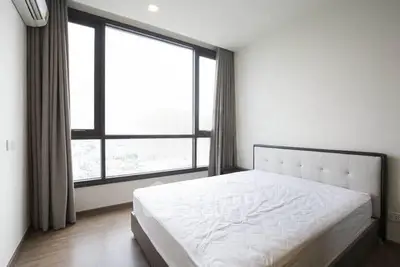 Spacious bedroom with large window offering natural light and city views, featuring a modern bed and elegant curtains.