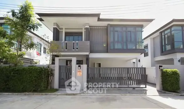 Modern two-story house with sleek design and gated entrance in a suburban neighborhood.