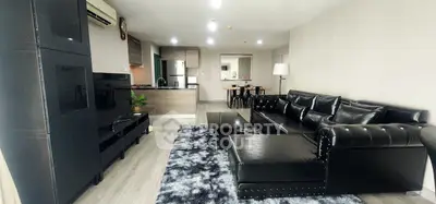 Spacious modern living room with black leather sofa and open kitchen layout