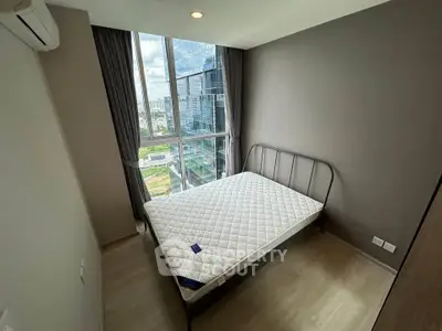 Modern bedroom with large window offering city view, featuring a minimalist bed and neutral decor.