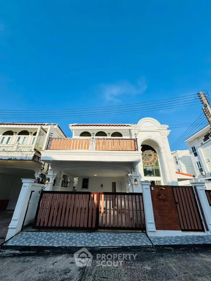 Stunning two-story white house with elegant balcony and gated entrance, perfect for luxurious living.