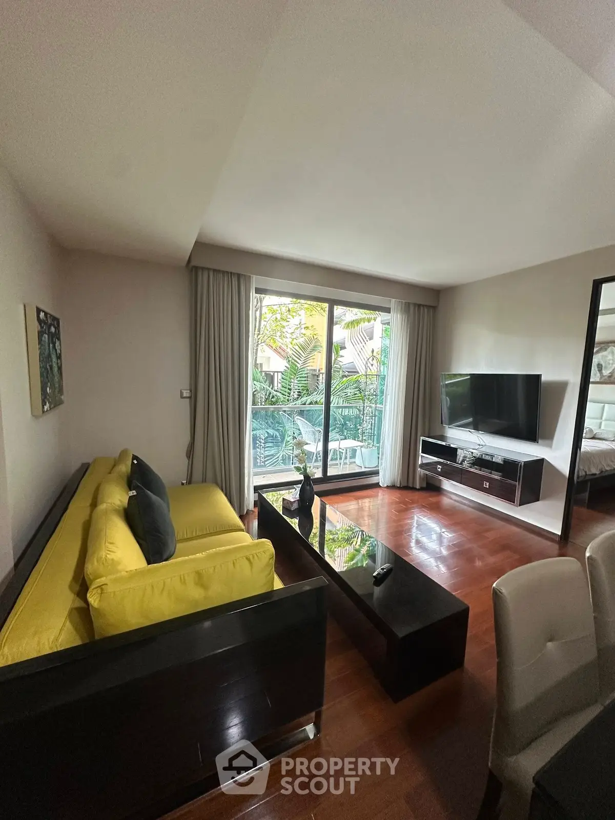 Stylish living room with vibrant yellow sofa and modern decor, overlooking lush greenery through large glass doors.