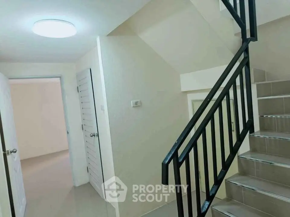 Modern staircase in a residential building with sleek black railing and bright lighting.
