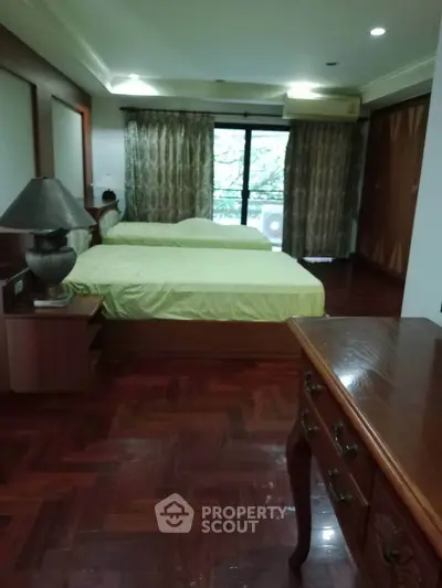 Spacious bedroom with elegant wooden flooring and twin beds, featuring a large window with lush green view.