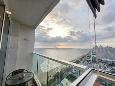 Stunning ocean view from high-rise balcony with glass railing and cozy seating area.