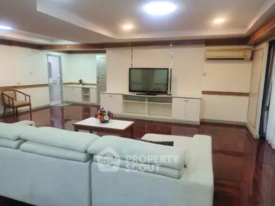 Spacious living room with modern decor and large sofa, featuring a flat-screen TV and elegant wooden flooring.
