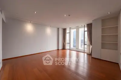 Spacious empty living room with hardwood floors and large windows offering city views.