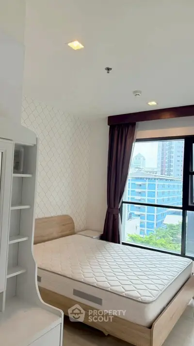Modern bedroom with large window and city view, featuring a comfortable bed and stylish decor.